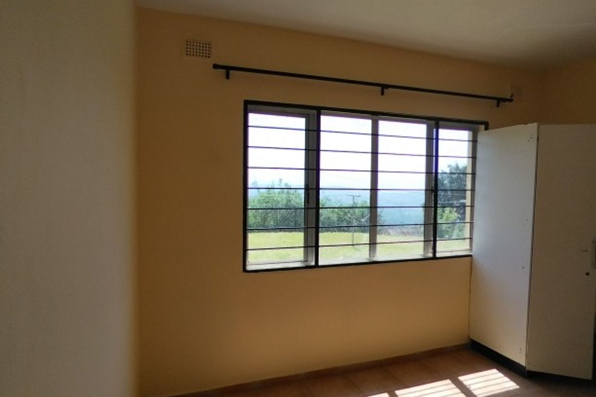 A simple, empty bedroom featuring tiled flooring, a large window with security bars, and neutral wall paint, offering a blank canvas for personalization.