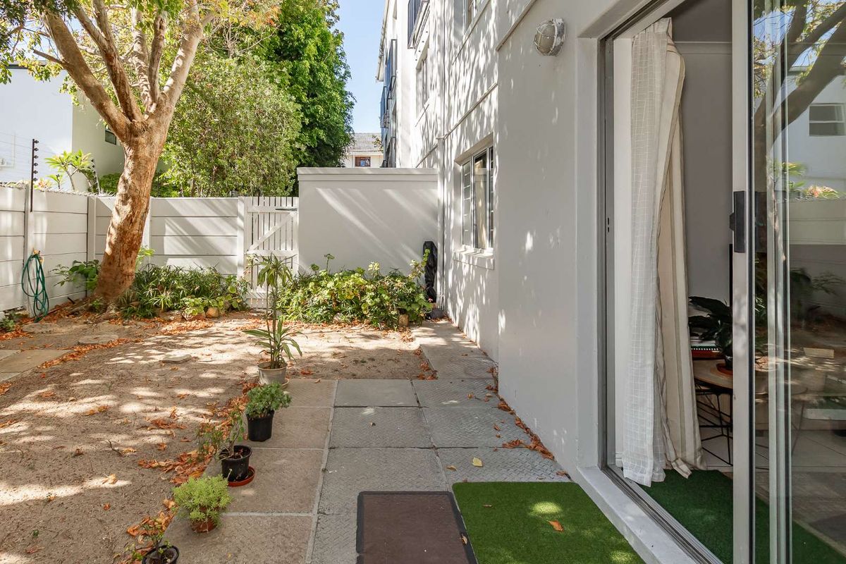 A private rear garden area featuring a paved walkway, perimeter walling, and direct access to the interior via sliding glass doors.
