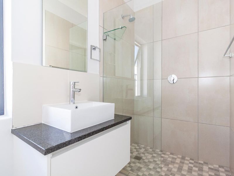Modern bathroom featuring a floating vanity with stone countertop, vessel sink, and a spacious walk-in shower with glass enclosure and neutral wall tiling.