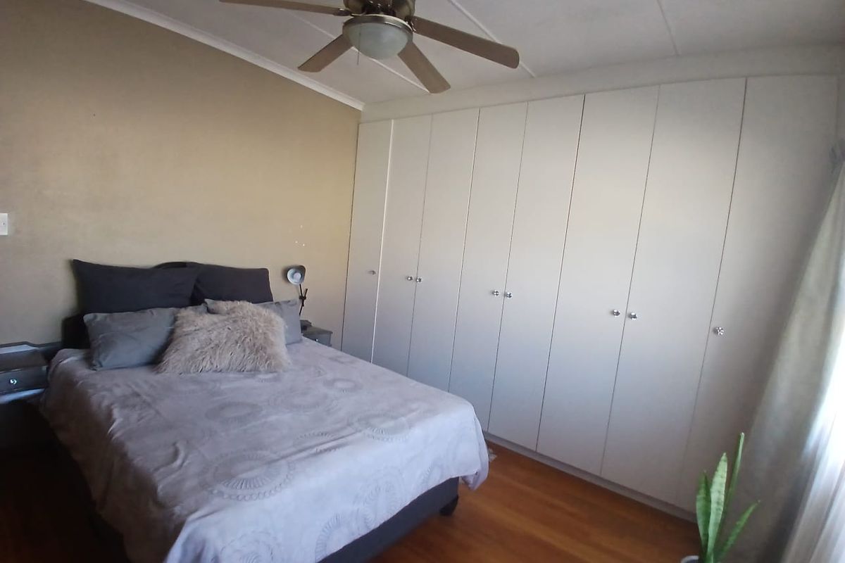 A bedroom featuring polished wooden flooring, a large wall-to-wall built-in wardrobe, and a ceiling fan.