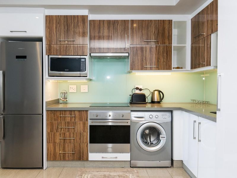 Modern kitchen featuring wood-grain and white cabinetry, stone countertops, glass splashback, and integrated appliances including an oven, hob, and washing machine.