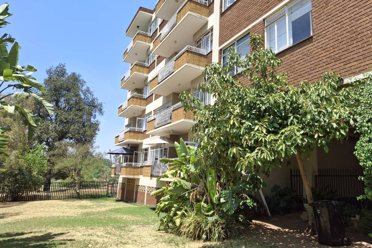 Exterior view of a multi-story apartment building featuring brick facade, private balconies with metal railings, and surrounding garden area.