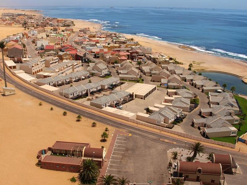 An aerial view of a coastal residential estate situated between the desert landscape and the ocean, showcasing the layout and proximity to the beach.
