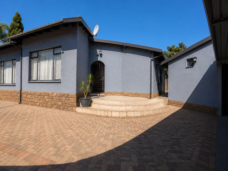 Front exterior view of the house featuring a paved driveway, stone-clad base, and tiled entrance steps leading to a secure doorway.
