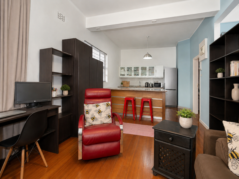 An open-plan living and kitchen area featuring hardwood flooring, a functional kitchen island with stone countertops, and built-in cabinetry.