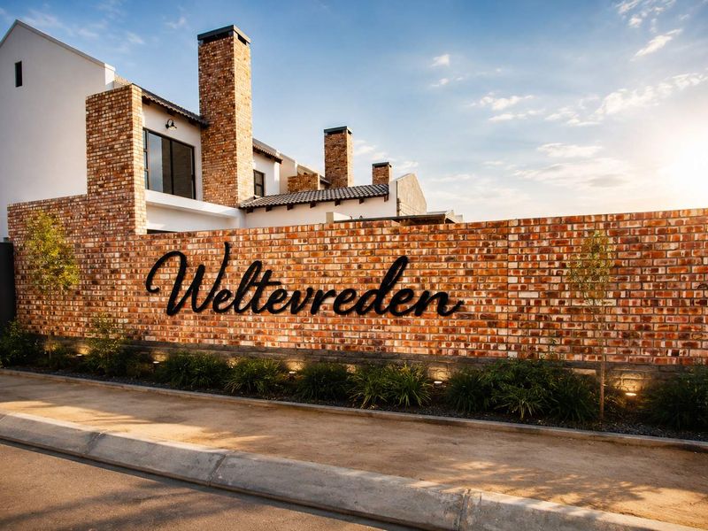 A well-maintained townhouse complex entrance featuring a prominent brick boundary wall with custom signage and integrated exterior lighting.