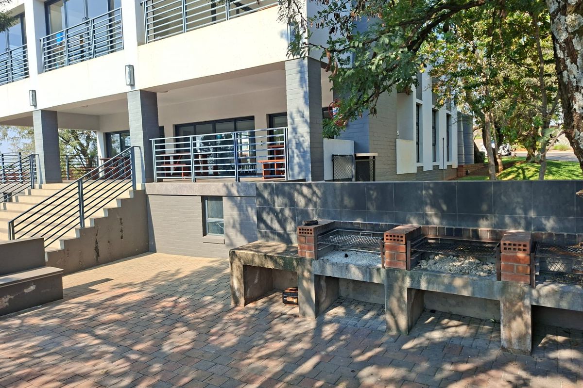 Rear exterior view of the apartment building featuring a paved patio area with a built-in brick braai and metal staircase access to the upper level.