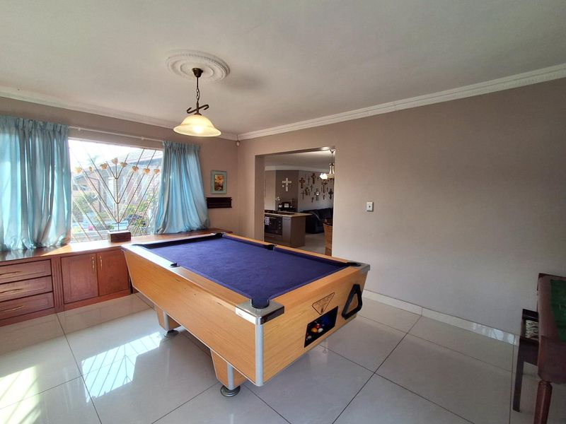 A living area featuring large format floor tiles, built-in cabinetry, and decorative ceiling coving, with an open transition to the adjacent kitchen space.
