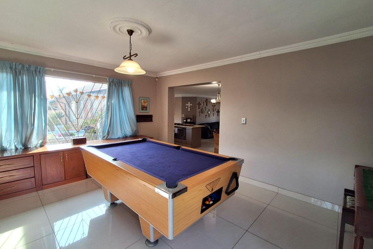 A living area featuring large format floor tiles, built-in cabinetry, and decorative ceiling coving, with an open transition to the adjacent kitchen space.