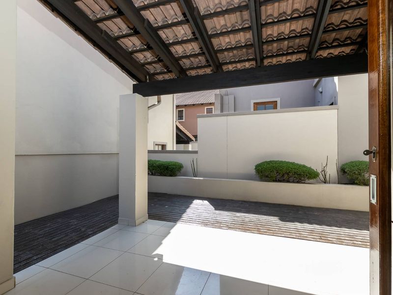 A covered patio area featuring a combination of tiled flooring and timber decking, complete with built-in raised planter beds.