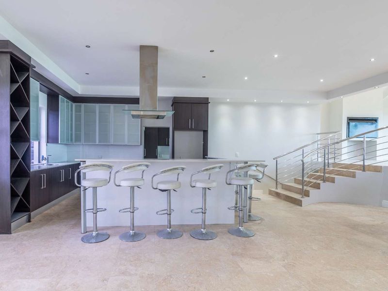 Spacious open-plan kitchen featuring modern cabinetry, a central island with breakfast bar, and a sleek staircase with stainless steel railings.