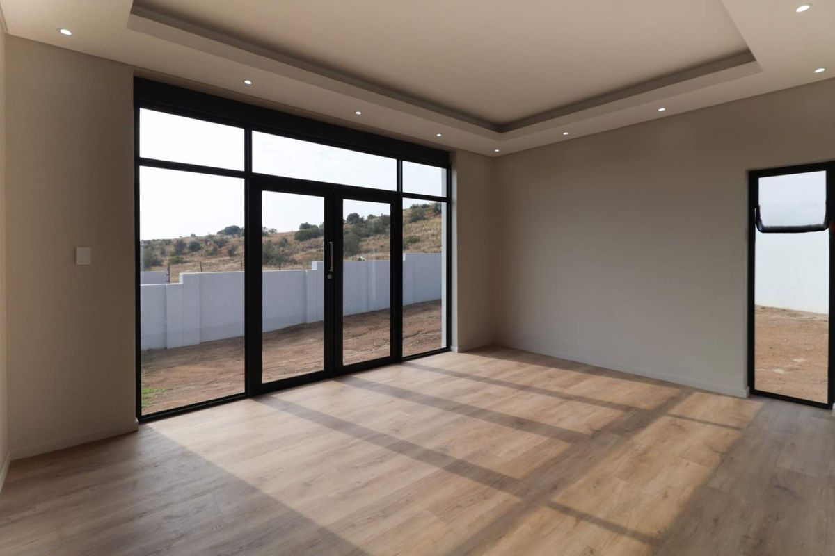 A bright, modern living area featuring high ceilings with recessed lighting, large black-framed glass doors, and light wood-look flooring.