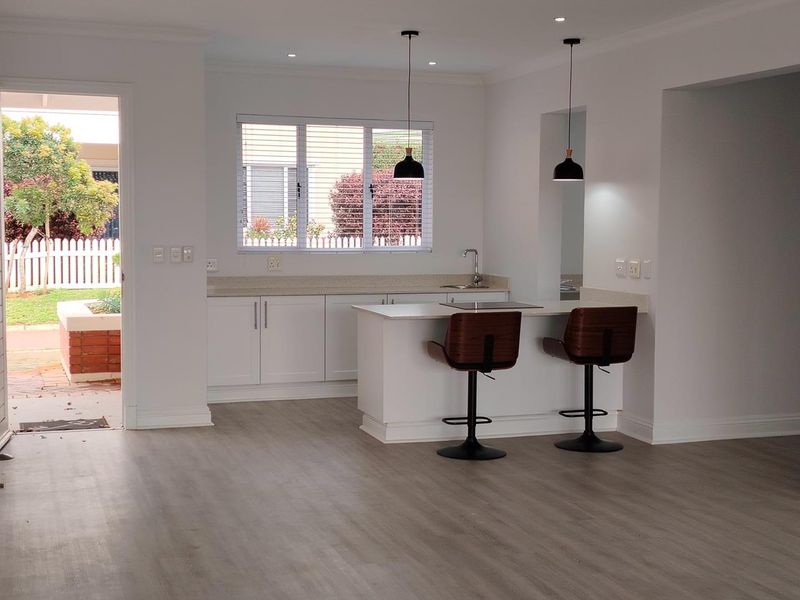 Modern open-plan kitchen featuring white cabinetry, stone countertops, a central island with integrated cooktop, and stylish pendant lighting, seamlessly connected to the living area.