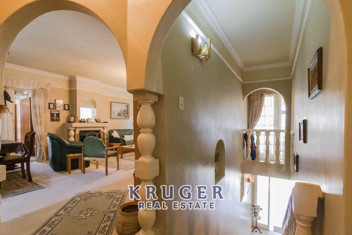 An interior view showing a living area with a fireplace, connected to a hallway with arched architectural details and a staircase.