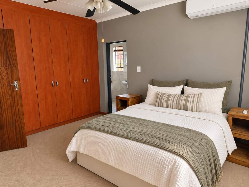 A well-maintained bedroom featuring extensive built-in wooden cupboards, neutral carpeting, a ceiling fan, and a wall-mounted air conditioning unit.