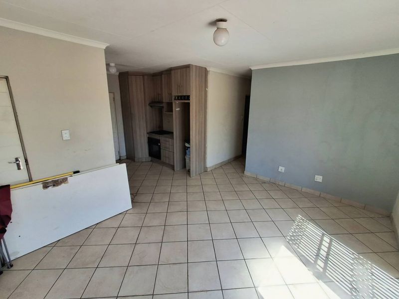 An open-plan living and kitchen area featuring tiled flooring, built-in cabinetry with an integrated oven, and neutral wall finishes.