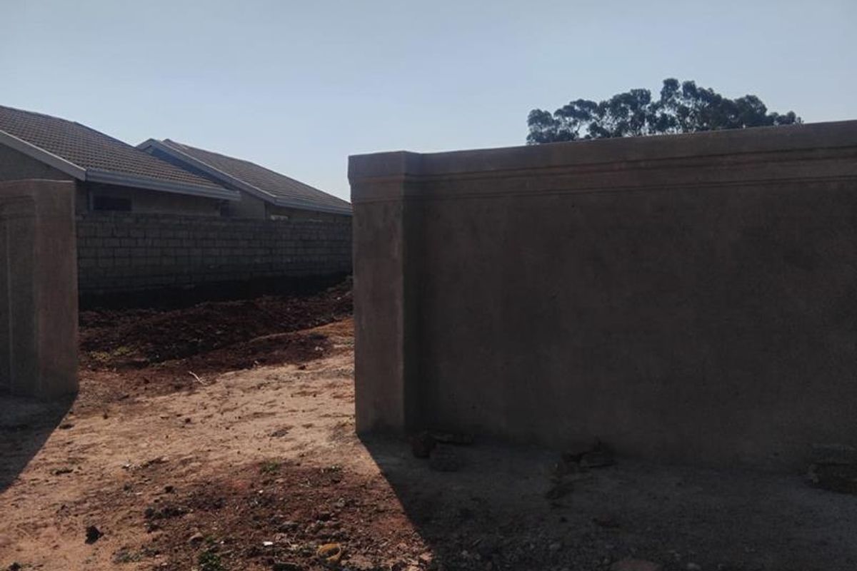 A view of a residential plot featuring a perimeter boundary wall and unpaved ground, showing the current state of the vacant land.