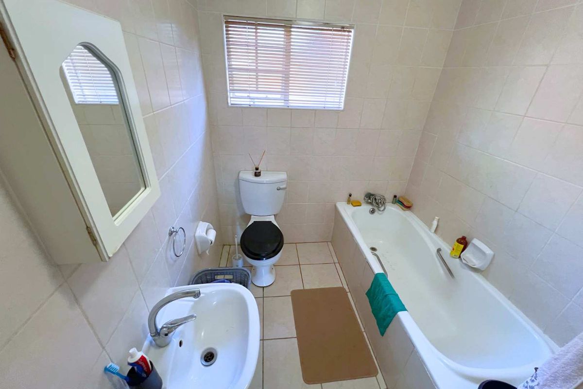 A functional bathroom featuring a standard bathtub, pedestal basin, and toilet, finished with neutral wall tiles and a window for natural light.
