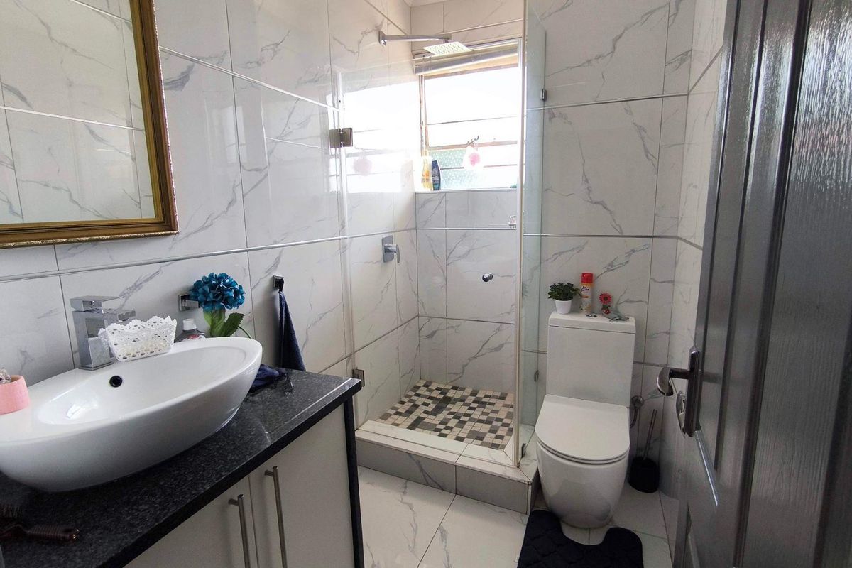 Modern bathroom featuring marble-look wall tiles, a glass-enclosed shower with mosaic floor tiling, a vanity with a granite countertop, and a ceramic toilet.