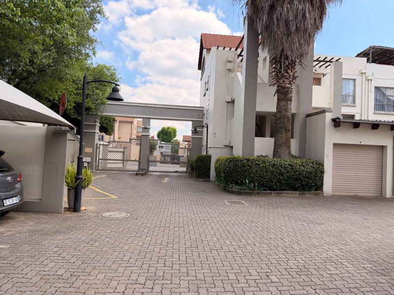 Front exterior view of the apartment complex featuring a paved driveway, secure gated entrance, and integrated garage access.