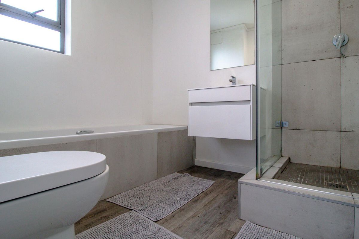 Modern bathroom featuring a floating vanity, glass-enclosed shower with concrete-look tiling, and a separate bathtub.