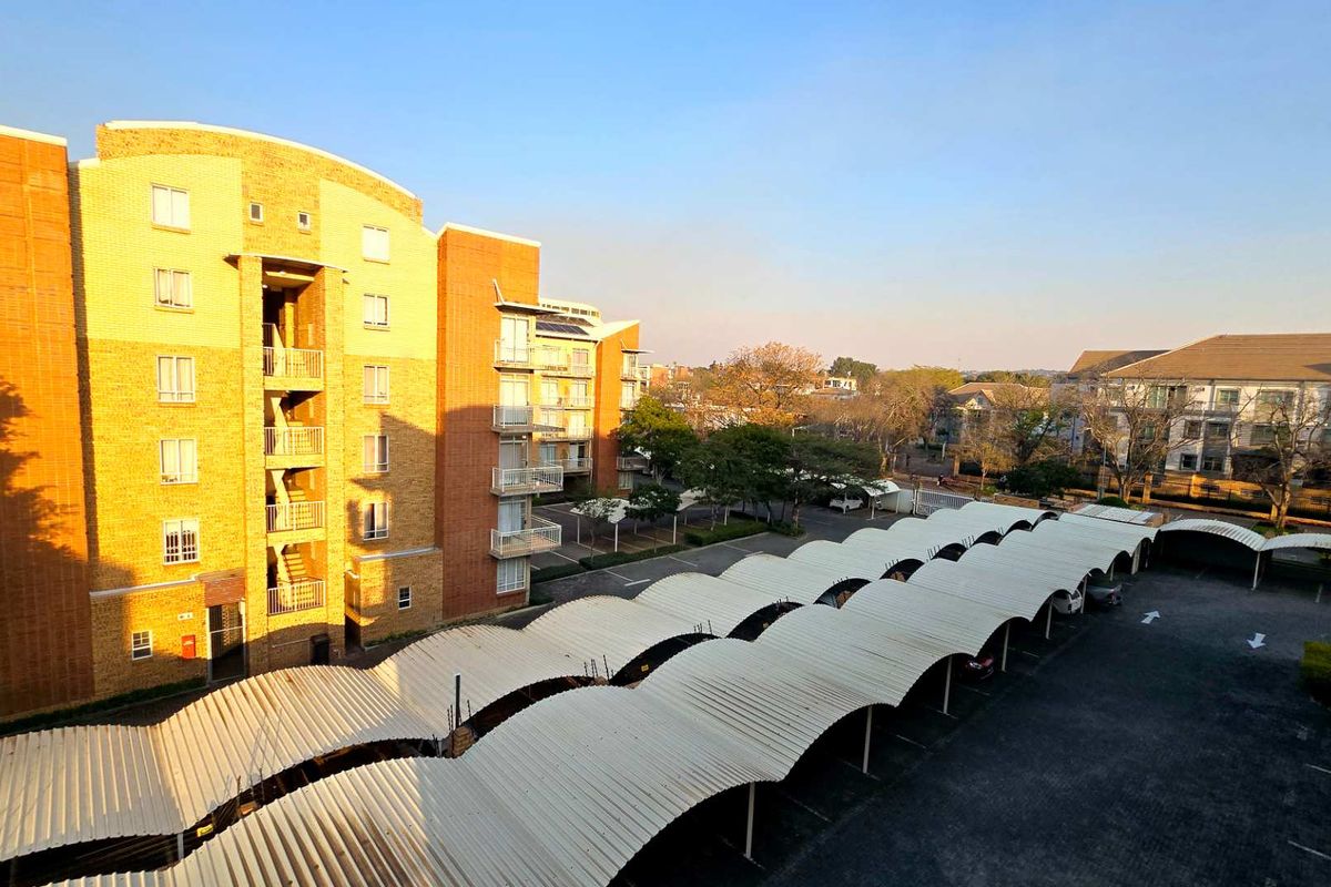 Elevated view of the apartment complex exterior, featuring covered parking bays and surrounding residential buildings.