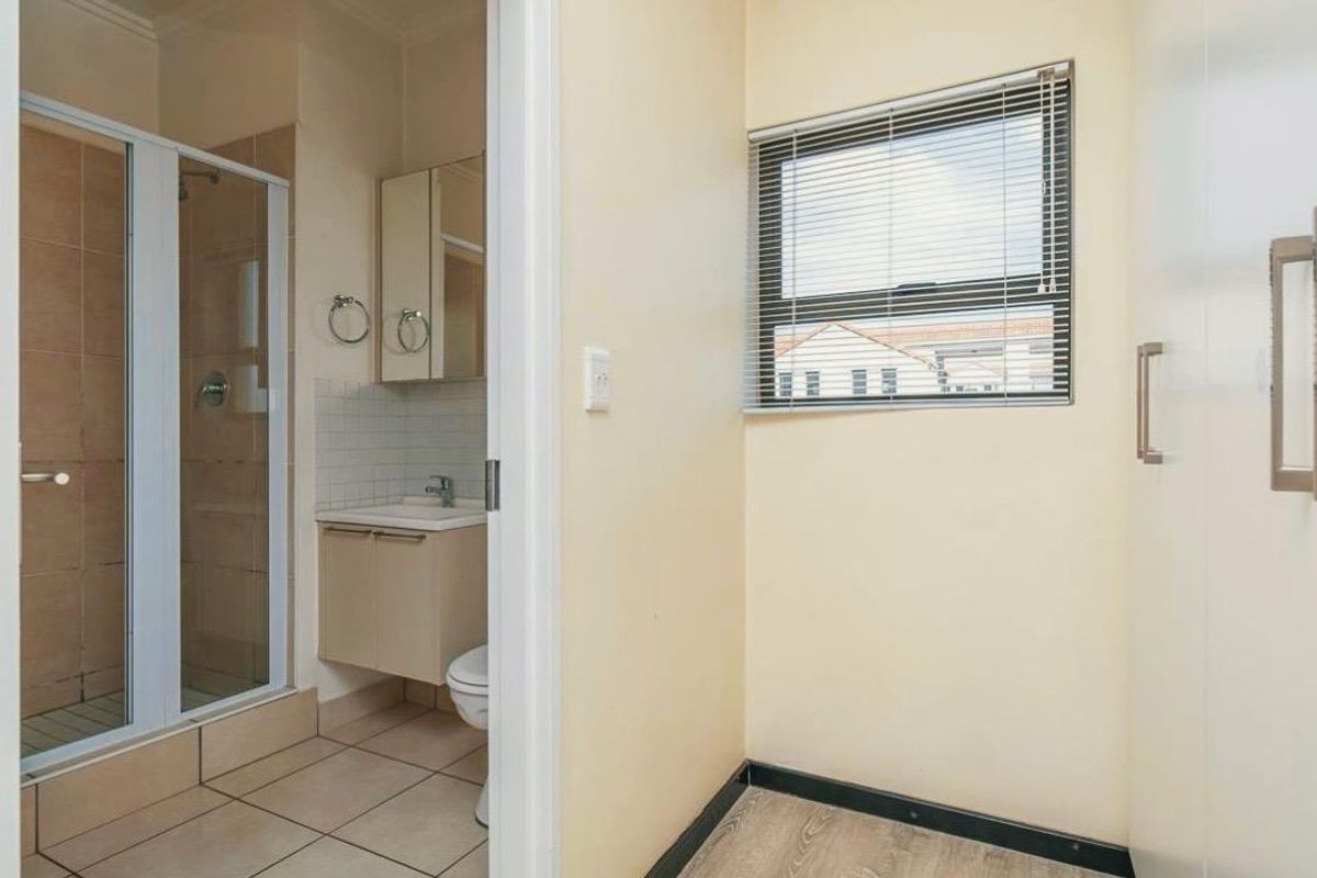 A functional bathroom featuring a glass-enclosed shower, vanity cabinet, and toilet, adjacent to a hallway area with built-in storage cupboards.