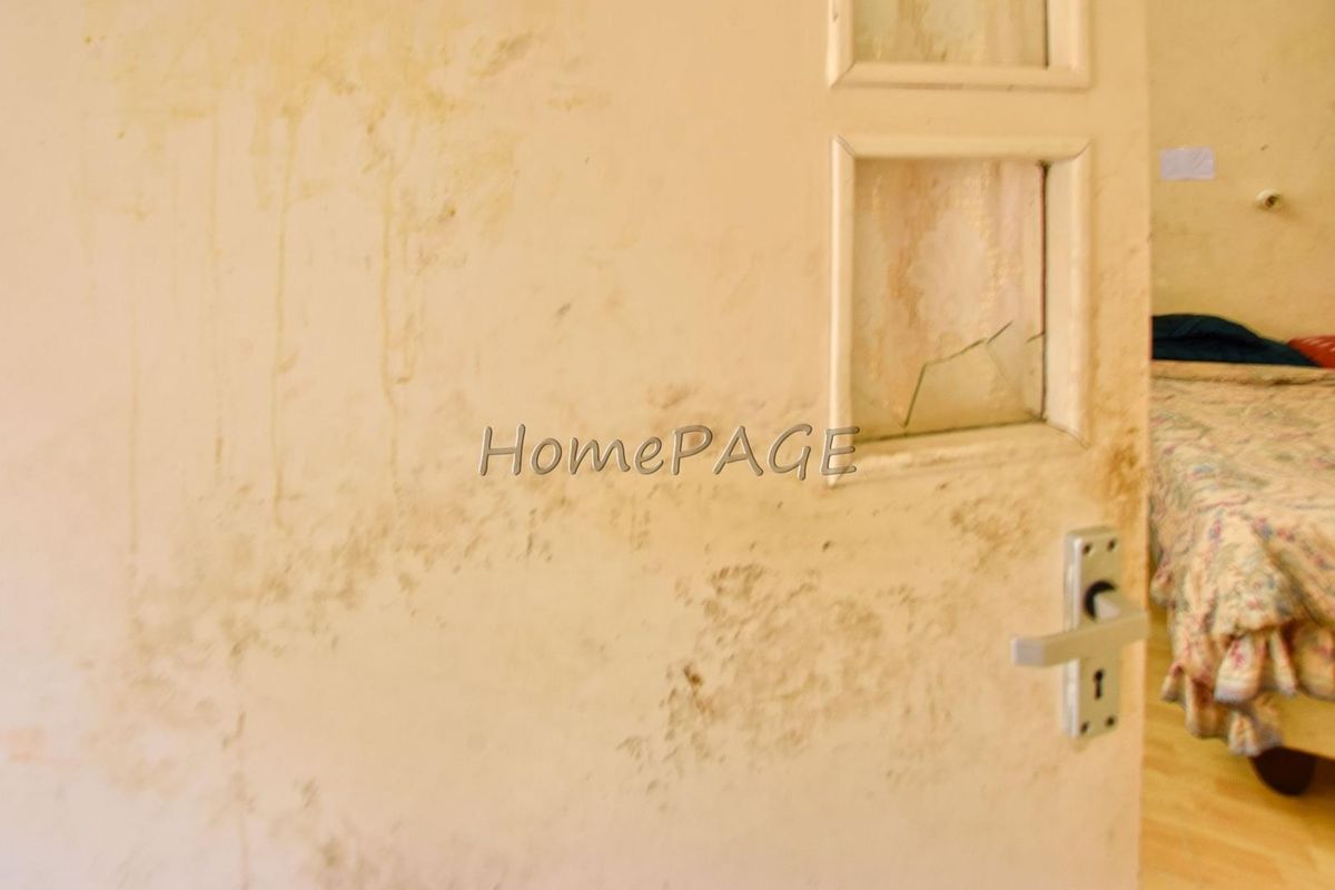 A bedroom interior featuring a damaged door with a cracked glass panel and significant wall staining requiring maintenance and refurbishment.