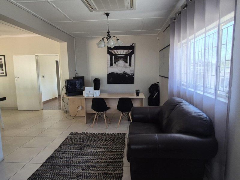 A functional living area featuring tiled flooring, a ceiling light fixture, and a window fitted with security bars.