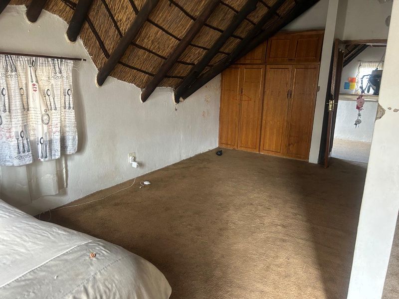 A bedroom featuring a vaulted thatched roof, built-in wooden cupboards, and carpeted flooring, offering a rustic attic-style living space.