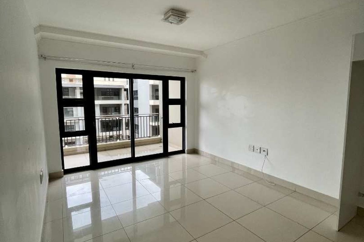 A bright, empty living room featuring large black-framed sliding glass doors that open onto a balcony, finished with neutral floor tiles.
