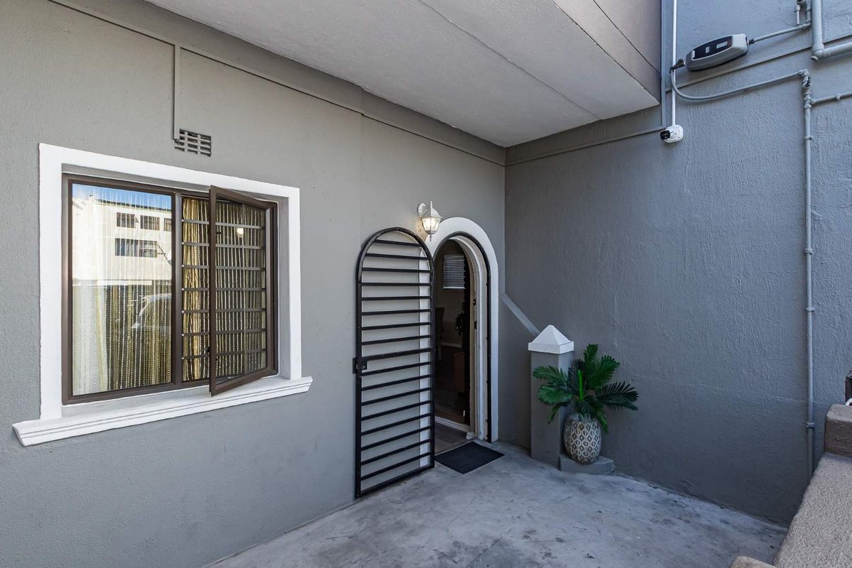 A private rear courtyard area featuring a concrete patio, secure entrance with a metal gate, and a window with security bars.