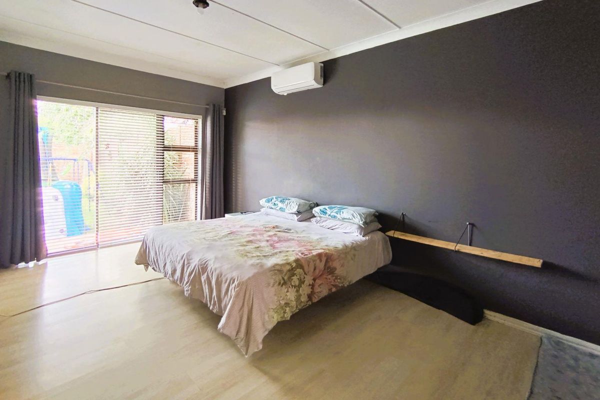 Spacious bedroom featuring light-toned flooring, a dark accent wall, a wall-mounted air conditioning unit, and sliding glass doors providing access to the garden.