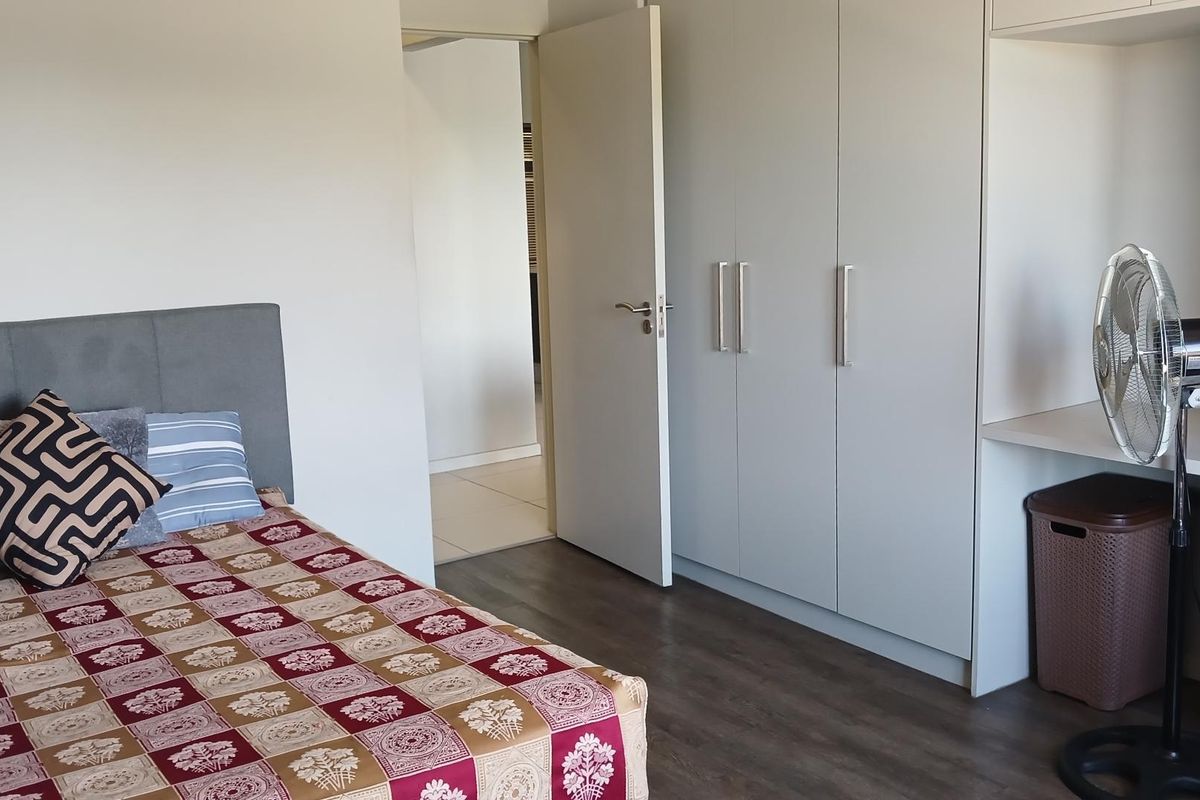 A bedroom featuring built-in cupboards, a desk area, and dark wood-look flooring, leading into a hallway.