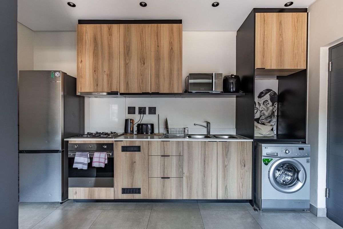 Modern kitchen featuring wood-grain cabinetry, integrated gas hob, oven, stainless steel sink, and dedicated space for a washing machine.