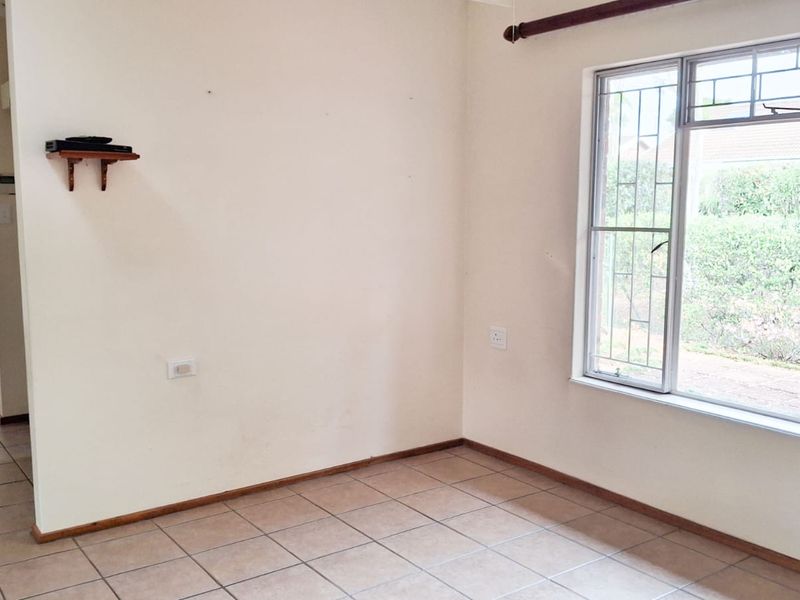An empty living room featuring tiled flooring, a large window with security bars, and neutral wall finishes, offering a blank canvas for interior design.