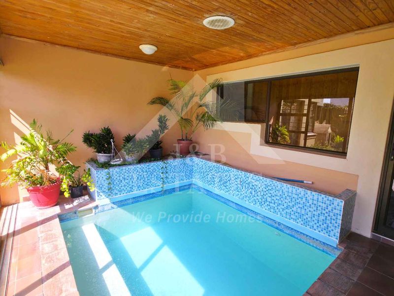 Covered indoor-outdoor pool area featuring a mosaic-tiled plunge pool, timber ceiling, and direct access to the garden through sliding glass doors.