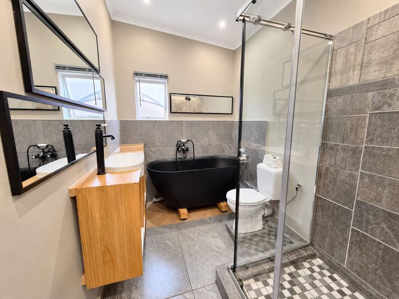 Modern bathroom featuring a sleek black freestanding bathtub, glass-enclosed shower, wood-finish vanity with vessel sink, and contemporary grey tiled finishes.