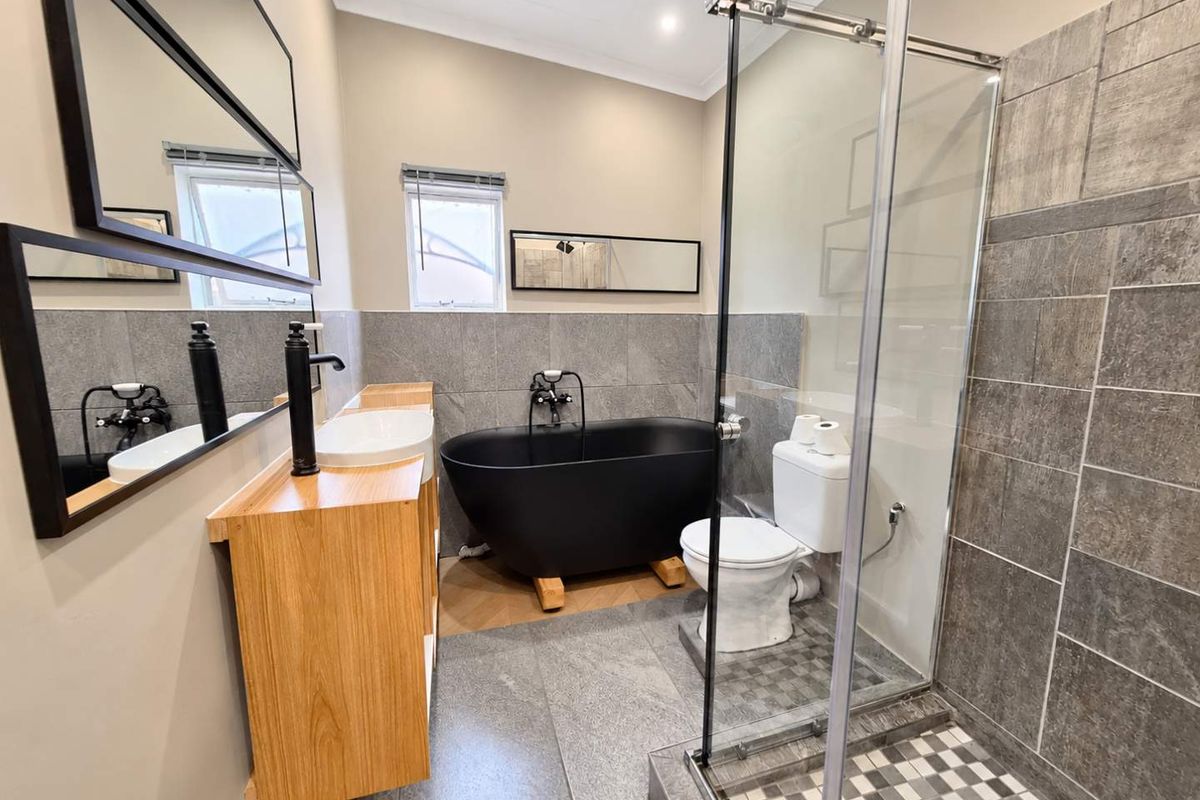 Modern bathroom featuring a sleek black freestanding bathtub, glass-enclosed shower, wood-finish vanity with vessel sink, and contemporary grey tiled finishes.