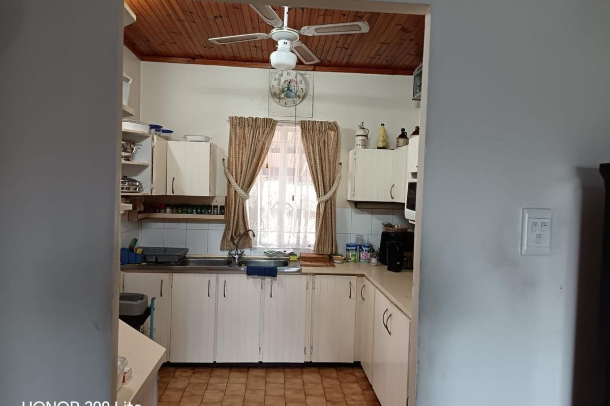 A dated kitchen featuring timber ceiling panels, white laminate cabinetry, tiled splashbacks, and a functional stainless steel sink area.