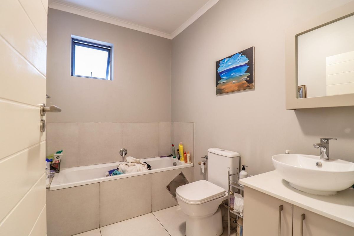 A functional bathroom featuring a built-in bathtub with tiled surround, a modern vessel sink vanity, and a standard toilet.