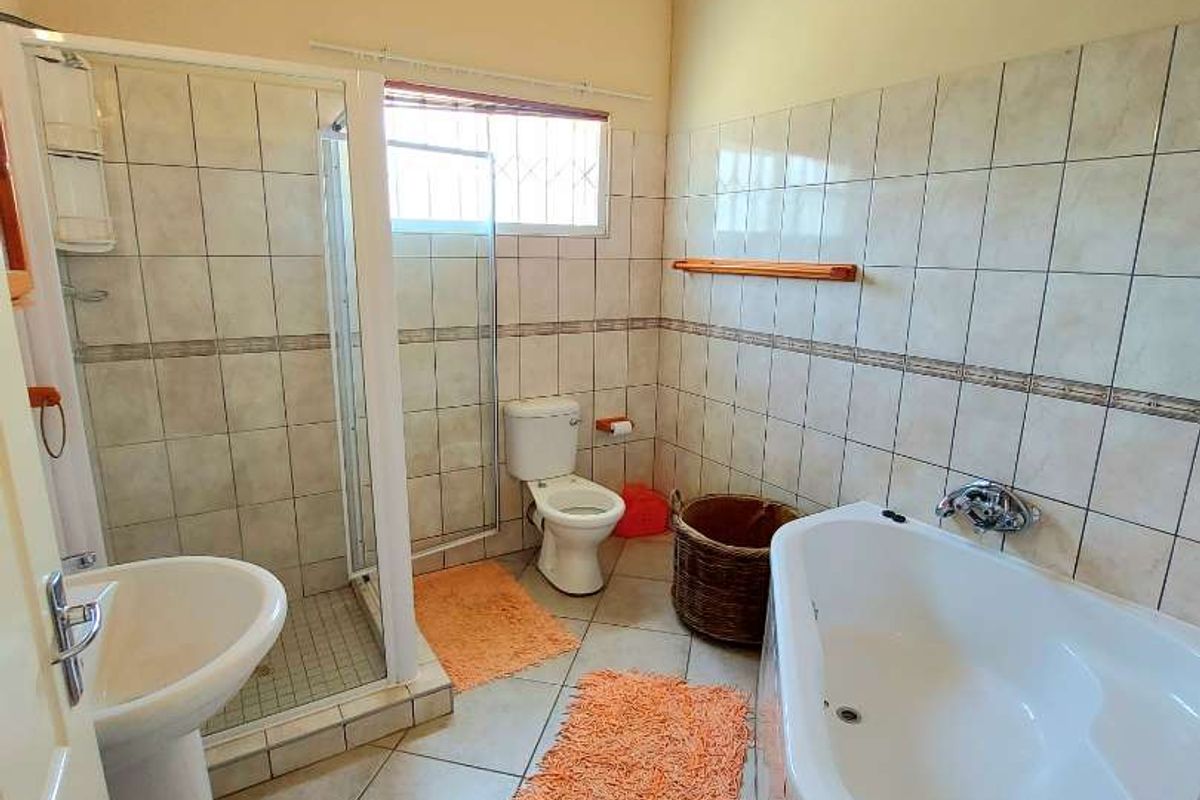A functional bathroom featuring a corner bathtub, separate glass-enclosed shower, pedestal basin, and toilet, finished with neutral wall tiles and a vaulted timber ceiling.