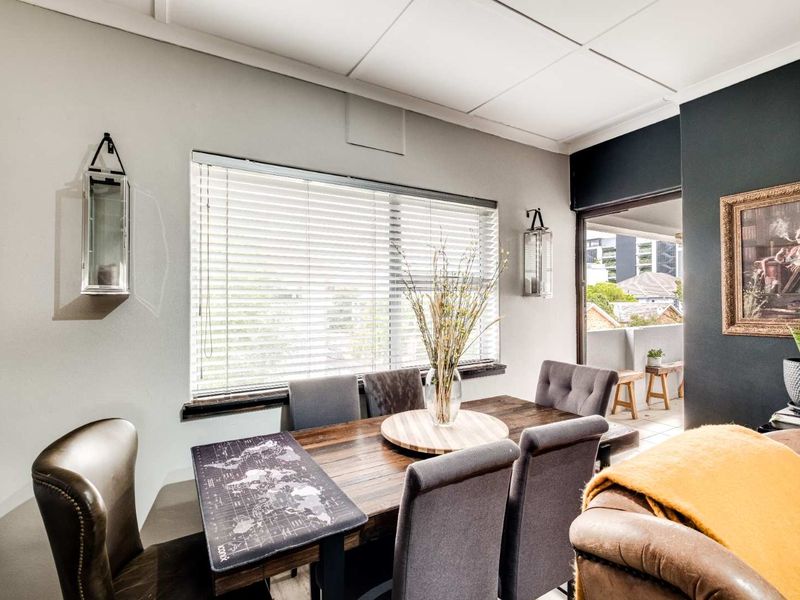 A well-lit dining area featuring a large window with venetian blinds and direct access to an outdoor balcony through a sliding glass door.