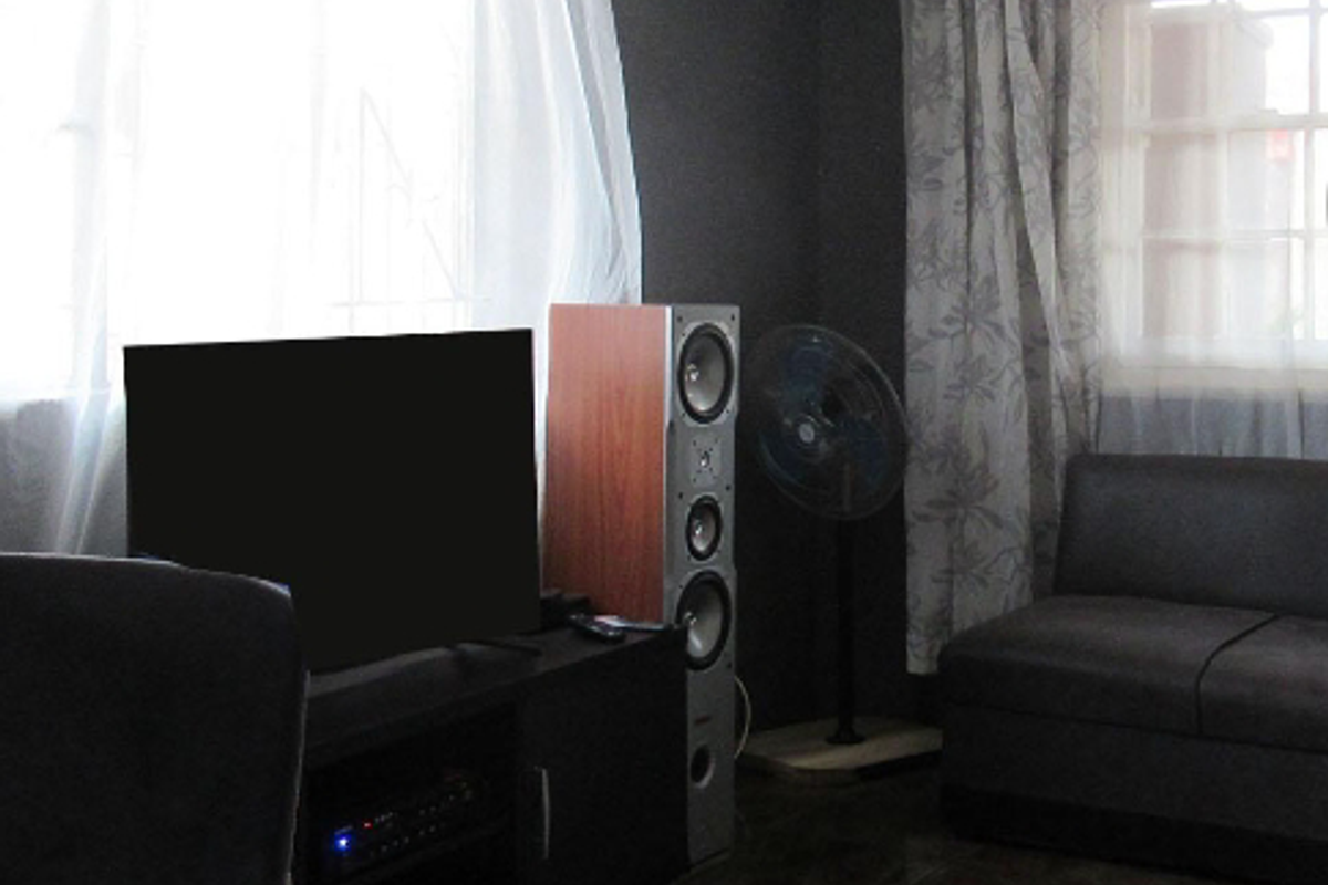 A living room area featuring dark wall finishes, tiled flooring, and large windows with curtains.