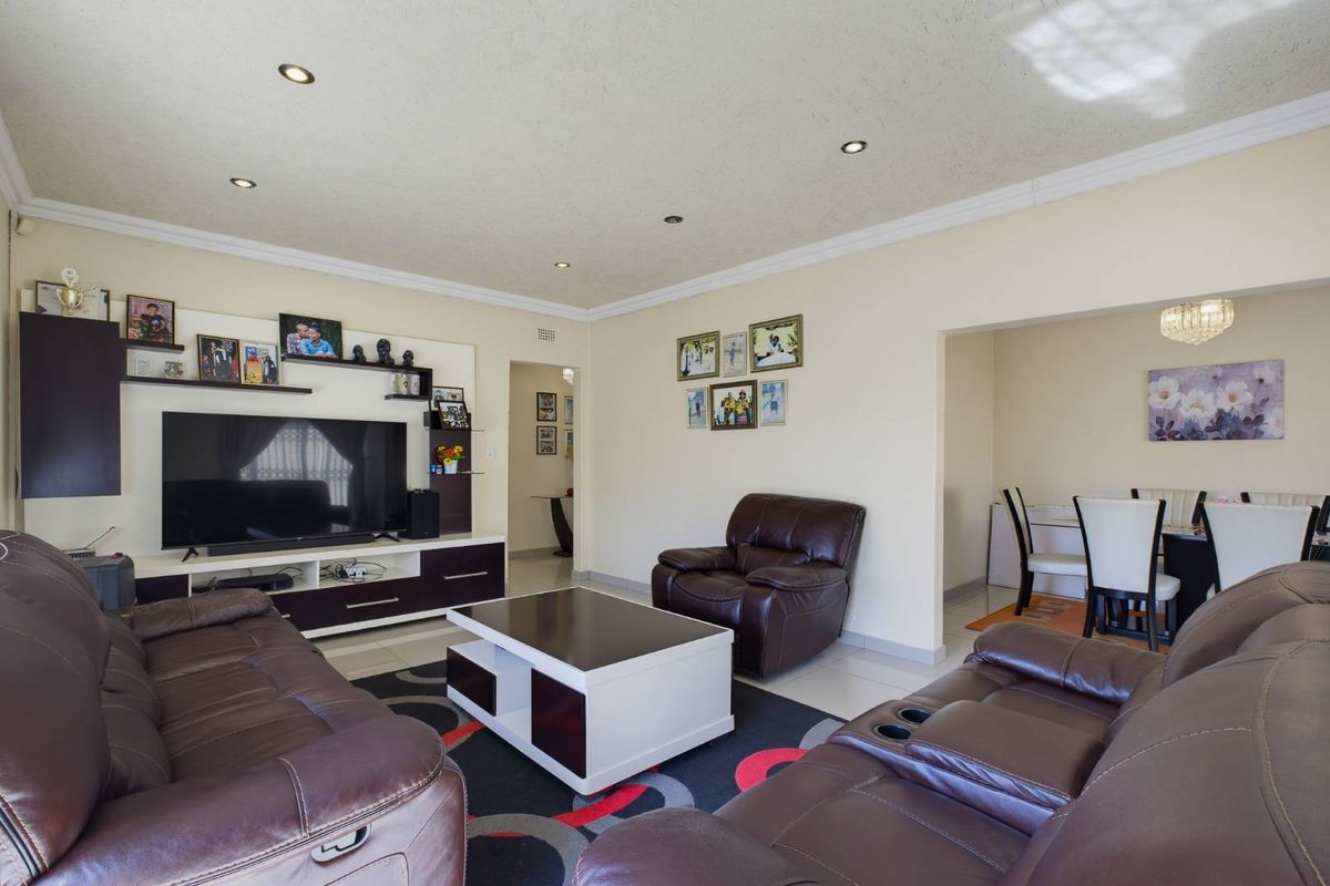A spacious living room featuring tiled flooring, recessed downlighting, and a coved ceiling, with an open-plan flow into the adjacent dining area.