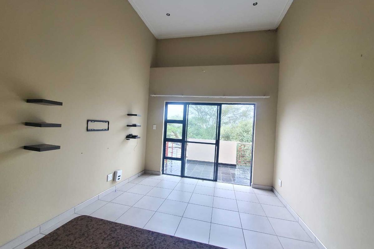 A bright, empty living room featuring high ceilings, tiled flooring, and large sliding glass doors that open onto a private balcony.