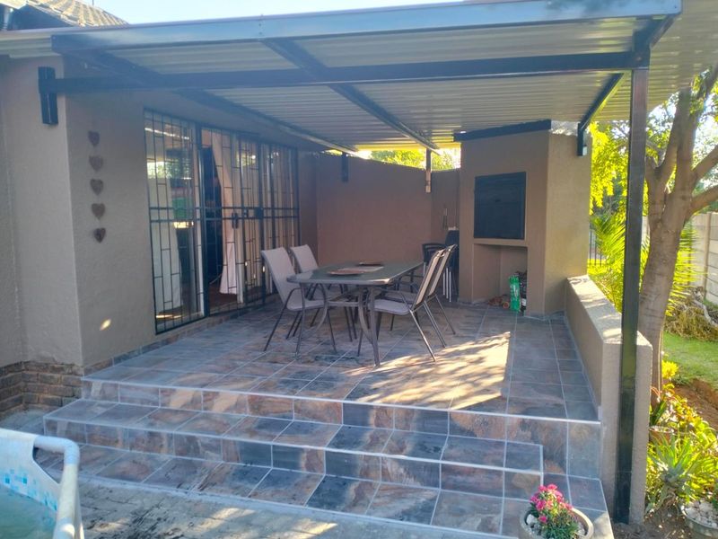 Covered patio area featuring tiled flooring and a built-in braai, providing a functional outdoor entertainment space.