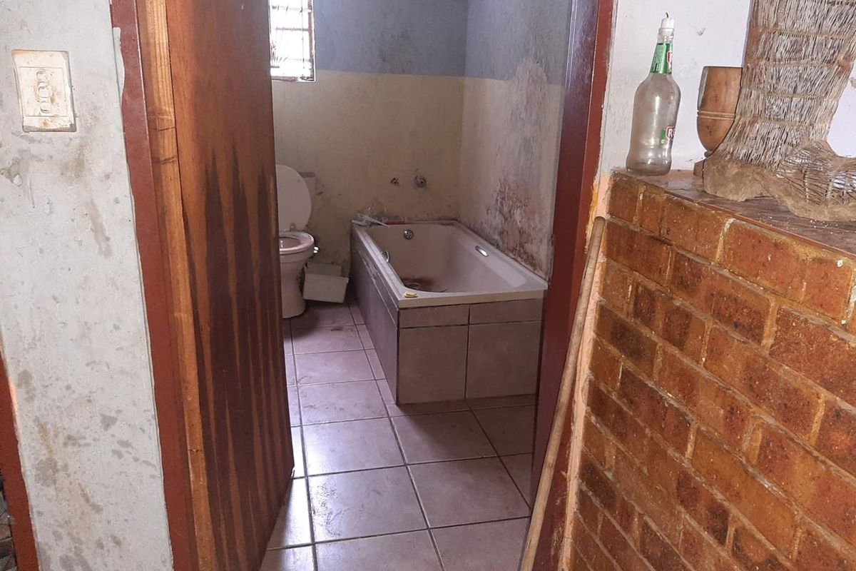 A dated bathroom featuring a built-in bathtub and toilet, requiring significant renovation and cosmetic updates to restore the space.