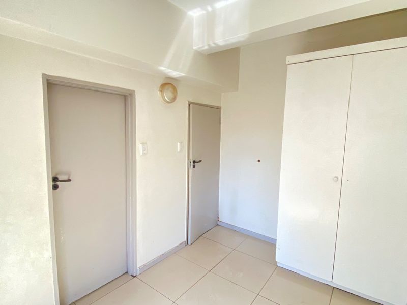 A functional hallway featuring tiled flooring, built-in cupboard storage, and neutral wall finishes, providing access to adjacent rooms.