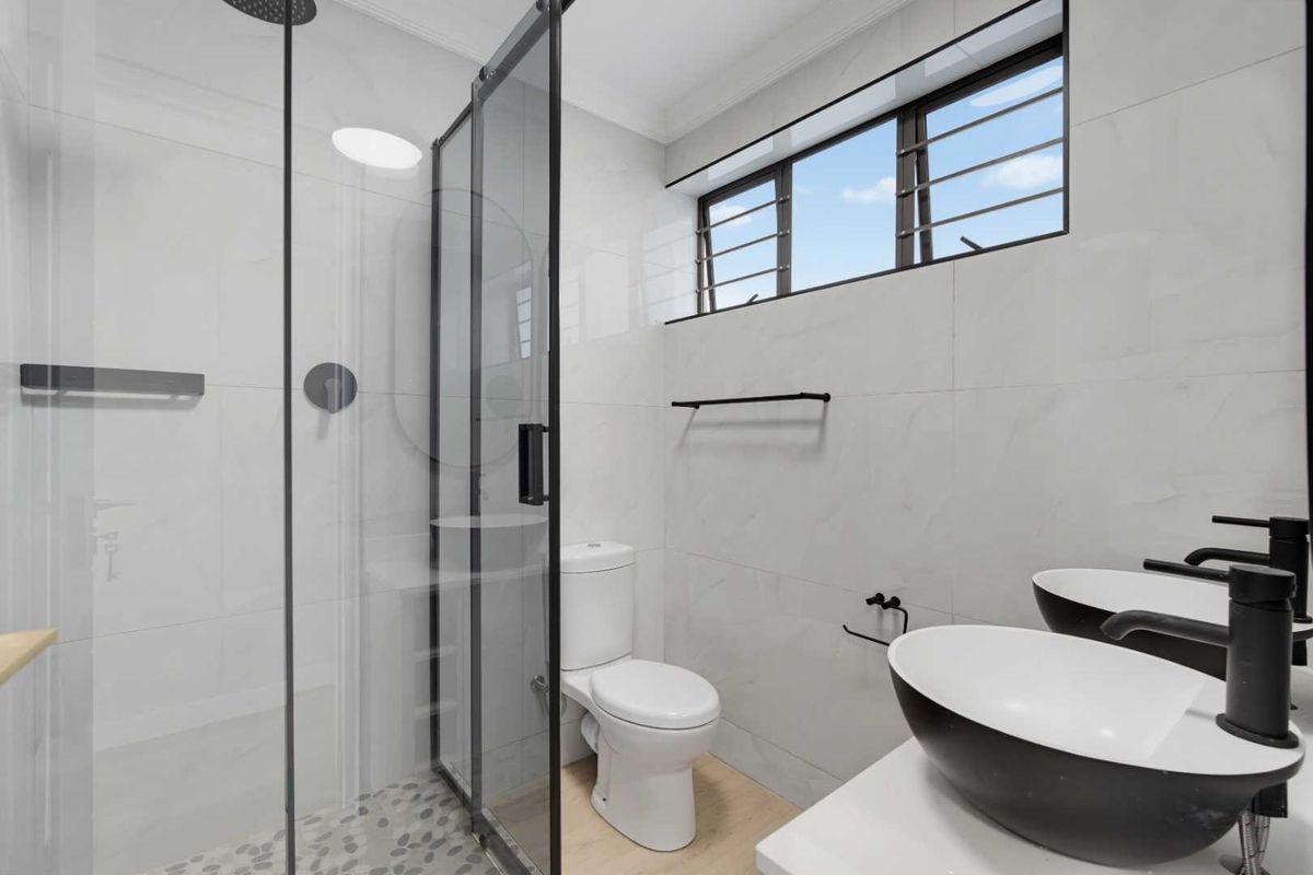 Modern bathroom featuring a glass-enclosed shower, dual vessel sinks with matte black fixtures, and neutral wall tiling.